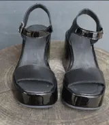 Sandalias negras de charol con plataforma y taco de cuña. Tira ancha sobre los dedos y pulsera con hebilla al tobillo.