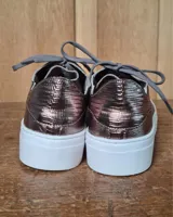 Zapatilla urbana de cuero con diseño combinado en color dorado metalizado y gamuza en tono tostado. Presenta cordones al tono, suela de goma blanca y detalles en cuero marrón en la parte posterior.