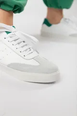 Zapatillas acordonadas de cuero color blanco con puntera de gamuza gris y detalles en verde.