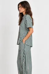 Blusa de algodón a rayas verde oscuro y blanco, con mangas cortas, cuello mao y detalle de botones tipo alamar en el frente. Presenta aberturas laterales en el ruedo.