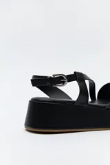 Sandalia negra con plataforma, tiras cruzadas sobre el empeine y pulsera ajustable al tobillo.