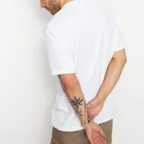 Remera blanca de manga corta con estampa central del logo de la marca éS sobre un fondo con textura de mármol.