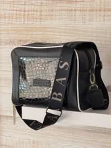 Bandolera negra de cuero con textura de cocodrilo, correa ancha con el nombre de la marca y detalles en blanco.
