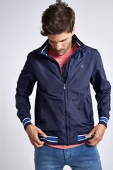 Campera liviana de nylon color gris oscuro, con cierre frontal completo, cuello subido y puños y cintura acanalados con rayas en rojo y blanco. Presenta logo bordado en el pecho y bolsillos laterales con cierre.