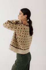 Buzo de tejido de punto con diseño de rombos en tonos beige y marrón. Presenta cuello polo con cierre frontal de tres botones, mangas largas con puños acanalados y ruedo también acanalado.