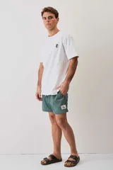 Short de baño verde con bolsillos laterales, cordón ajustable en la cintura y parche decorativo en la pierna izquierda.