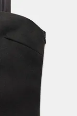 Vestido midi de escote recto con hombros descubiertos y detalle de fular integrado al tono. Presenta un cuerpo estructurado y una falda inferior semitransparente con diseño plisado. Cierre lateral con cremallera oculta.