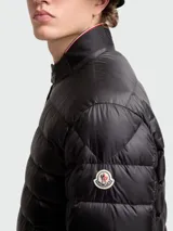 Campera corta de plumas Moncler modelo Rigel, color negro, con diseño acolchado horizontal, cuello alto con cierre de broches y cierre frontal completo.