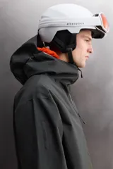 Cazadora deportiva de esquí con diseño bicolor en tonos negro y verde oliva. Presenta capucha amplia con visera, cierre frontal con cremallera termosellada, bolsillos frontales y en manga con cierres impermeables, y aberturas de ventilación en las axilas. Incluye faldón interior antinieve, puños ajustables y tecnología de rescate RECCO.