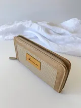 Billetera grande con cierre metálico, color beige. Presenta un panel central con textura tejida o tramada en tono claro y bordes de cuero liso en tono beige más oscuro. Posee un parche de cuero con la palabra "chouie" escrita a mano.