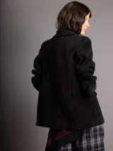 Blazer de corte clásico en color negro, con solapas, hombreras y cierre frontal con un botón. Presenta una textura acanalada similar al terciopelo y bolsillos decorativos en el frente.