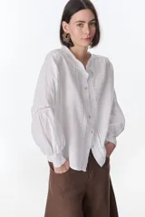 Camisa celeste de lino con botones, mangas largas abullonadas y detalles de crochet en el frente y los puños.