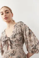 Vestido corto con estampado animal print en tonos beige y negro. Tiene mangas tres cuartos con elástico, cut-out en el frente y lazo.