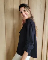 Blusa celeste de algodón con estampado de rayas verticales formadas por pequeños motivos blancos, escote en V con cuello alto fruncido y mangas largas abullonadas con puños amplios.