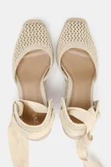 Alpargata de mujer con plataforma y taco cuña alto, confeccionada en rafia trenzada. La capellada es de tejido de punto calado color beige, con talón cerrado y tiras largas de tela para atar al tobillo.