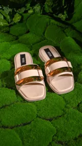 Sandalias chatas color beige con dos tiras anchas y hebillas doradas.