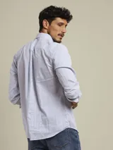 Camisa de manga larga con patrón de rayas verticales celestes y blancas, corte regular fit, cuello con botones y un bolsillo en el pecho con logo bordado.