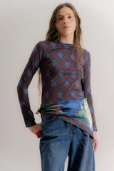 Remera de manga larga confeccionada en algodón elastizado, con cuello redondo y diseño ajustado al cuerpo. Presenta un estampado de rombos finos con motivos florales en tonos azules sobre una base de color marrón oscuro.