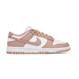 Zapatilla Nike Dunk Low, silueta de corte bajo, con base de cuero blanco y superposiciones en cuero color rosa pálido/nude. Presenta el logo Swoosh lateral en el mismo tono rosa pálido y suela de goma blanca y rosa pálido.