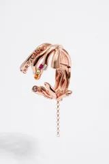 Pulsera ancha rígida de metal color oro rosado con diseño de manos entrelazadas adornadas con strass y gemas de colores.