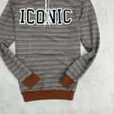 Canguro rústico a rayas horizontales en tonos marrón y gris, con capucha forrada, puños y cintura en color marrón liso. Estampa frontal con la palabra "ICONIC" en letras blancas con borde negro.