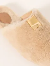 Pantuflas tipo slide color beige, confeccionadas en cuero de oveja con aplique metálico en el empeine, forrería de cuero caprino y suela de cuero vacuno.