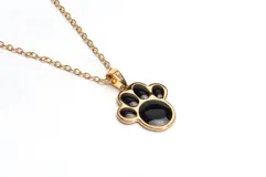 Collar con cadena dorada y dije con forma de huella de mascota, con borde dorado y relleno de esmalte negro.