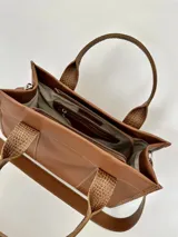 Cartera marrón de cuero genuino con doble asa corta y correa bandolera estampada con la frase "Chabas, soy real, no perfecta".