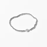 Pulsera elástica de cuentas plateadas con dije circular con pequeños cristales incrustados.