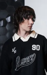 Sweater de punto negro con cuello polo en color crema, manga larga y diseño oversize. Presenta bordados en el frente con la inscripción 'Ravers', el número '90' y letras cursivas, con terminaciones en punto rib en puños y cuello.