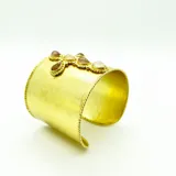 Brazalete dorado con forma de cruz adornada con piedras naturales.