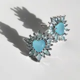 Par de aros plateados con forma de flor, con cristales celestes y cristal azulado en forma de corazón en el centro.