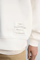 Sudadera negra de corte relaxed fit, confeccionada en tejido técnico interlock de algodón con elasticidad. Presenta cuello redondo, manga larga y una etiqueta aplicada en el bajo. Los acabados son en rib.