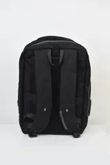 Mochila ejecutiva negra con diseño rígido y geométrico en el frente, asa superior y herraje metálico horizontal. Presenta un puerto USB lateral.