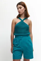 Top tejido color turquesa, sin mangas y con tirantes cruzados al frente que forman un nudo decorativo en el escote.