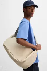 Bolso de hombro de diseño minimalista confeccionado en tejido de algodón. Cuenta con un compartimento principal con cierre de solapa con doble imán y botón a presión, además de bolsillos interiores. Incluye asa de hombro fija.