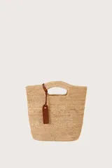 Bolso tipo basket de rafia natural, con asas integradas y detalle de etiqueta de cuero sintético marrón.