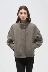 Campera de corte holgado en color gris, con cuello alto, cierre frontal oculto y mangas largas. Presenta costuras decorativas en el frente y bolsillos laterales.