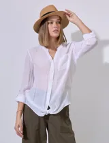 Camisa blanca de gasa con cuello a la base y escote en V, abertura central con botones, bolsillo aplicado en el pecho, mangas largas regulables con presilla y terminación anudada opcional.