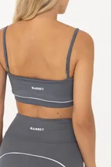 Top deportivo gris con breteles finos regulables y contorno inferior blanco.