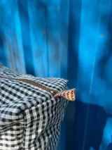 Necessaire con estampado a cuadros blanco y negro, grifa de goma, detalles de cordón, cierre y bolsillo transparente interior.