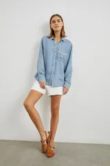 Camisa celeste de denim tencel, de corte holgado, con cuello clásico, cierre frontal con botones y bolsillo en el pecho con detalle bordado.