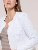 Chaqueta corta confeccionada en tejido bouclé texturizado de color blanco con sutiles lentejuelas. Presenta escote redondo, diseño abierto al frente, bolsillos frontales con solapa y mangas largas con puños de tela lisa.