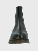 Botín chelsea negro de cuero con elásticos laterales, suela de goma gruesa y pespuntes amarillos alrededor de la suela. Tiene una tira trasera para facilitar el calce.