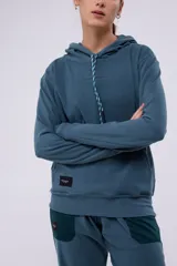 Hoodie azul con capucha y cordón blanco y verde. Tiene un pequeño logo estampado en el pecho y un parche con el logo de la marca en el lateral.