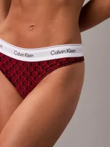 Conjunto de ropa interior Calvin Klein compuesto por un corpiño triangular y una bombacha colaless. Ambas piezas presentan un estampado de monograma de la marca en color rojo sobre fondo oscuro, con la banda elástica característica en color blanco con el logo de la marca en negro.