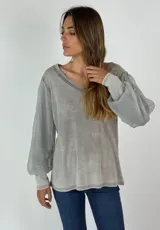 Blusa de manga larga color gris con efecto desgastado, cuello en V y mangas abullonadas de tela transparente.