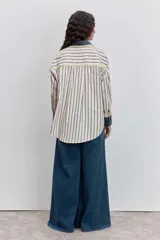 Camisa de corte oversize con estampado de rayas verticales, cuello clásico y cierre frontal de botones. Presenta dos bolsillos frontales en contraste con bordados de tréboles, además de puños y cuello en color sólido con detalles en amarillo.