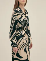 Vestido largo estilo camisero confeccionado en seda viscosa con estampado abstracto en blanco y negro. Cuenta con botones nacarados, bolsillos laterales, lazo para ajustar en la cintura y aberturas laterales.