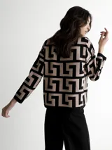 Sweater de punto con cuello redondo y mangas 3/4. Diseño con motivos geométricos en color visón y negro. Incluye una bufanda fina con estampado a cuadros en tonos marrones.